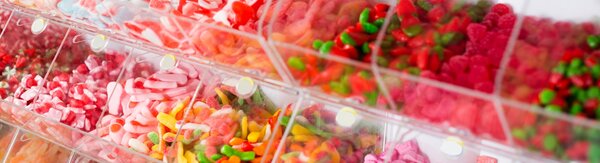 Eine Selbstbedienungstheke mit zahlreichen offenen Fächern, die bunt gemischte Süßigkeiten wie Gummibärchen und Fruchtgummi enthalten.