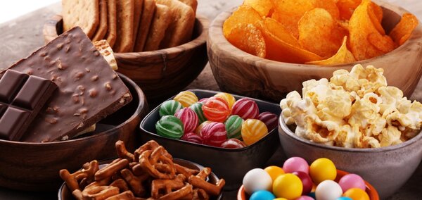 Verschiedene Snacks wie Schokolade, Chips, Salzstangen, Popcorn, Kekse und bunte Süßigkeiten sind in Schalen angerichtet.
